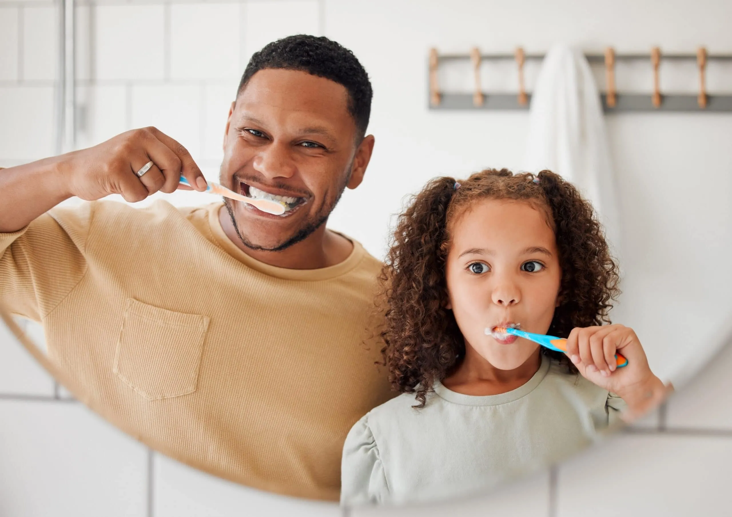 Father and daughter brushing their teeth together, emphasizing oral hygiene and family bonding in a bathroom setting.
