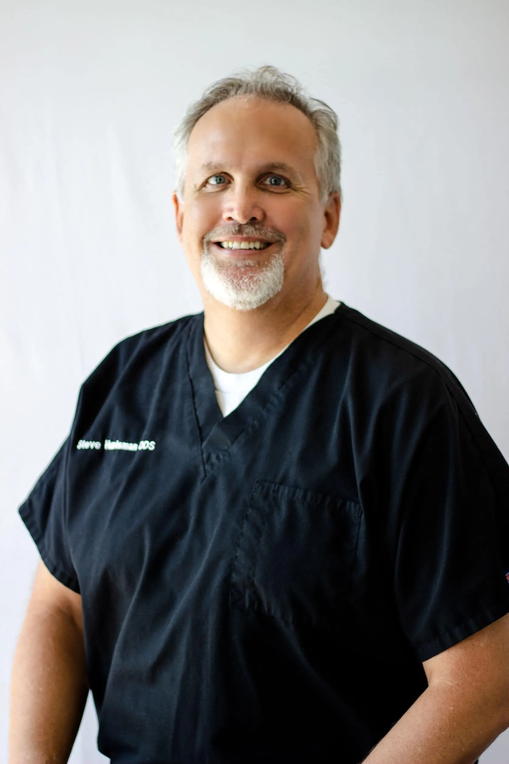 Dr. Steve Huntsman, orthodontist at Ortho:Dana, smiling in professional black scrubs, showcasing expertise in orthodontics and commitment to patient care.