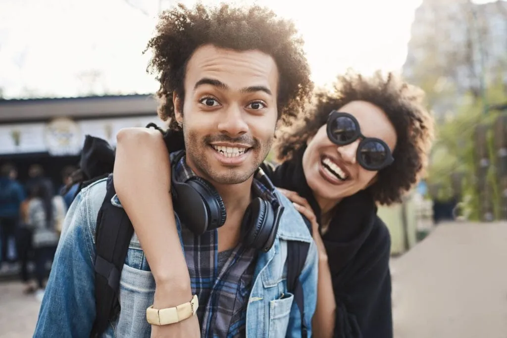 African American couple smiling and hugging while walking in a park, expressing joy and confidence, reflecting the positive emotions associated with Invisalign Teen treatment at Ortho:Dana.